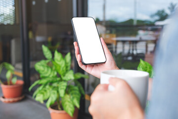 Mockup image of a woman holding coffee cup and mobile phone with blank white desktop screen