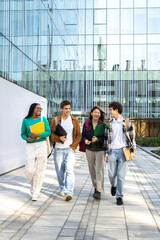 Vertical image of multiracial happy university students walking to class together laughing and...