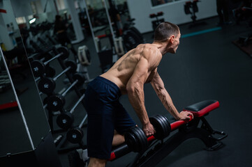 Shirtless man doing dumbbell row to waist on bench at gym. 