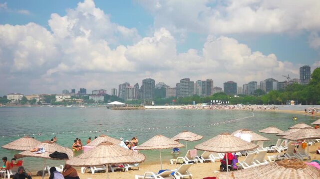 People resting on the Caddebostan sandy beach. Citizens swimming and sunbathing under umbrellas on summer sunny day. Asian side of Istanbul city in the background