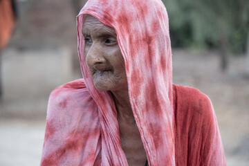 A helpless elderly woman with a sad, pained expression sits in a refugee camp