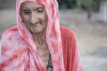 A helpless elderly woman with a sad, pained expression sits in a refugee camp