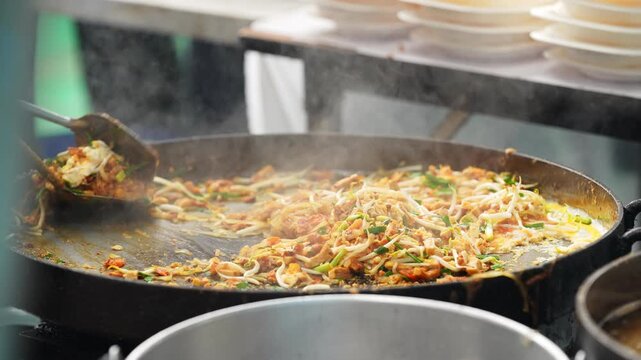 Cooking the famous Thai street food dish called 'Pad Thai', which is a stir fried dish of noodles, bean sprouts, vegetables with chicken or prawns, wrapped in a thin omlette.