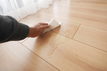 hand wiping spilled tea with paper napkin on floor ,