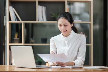 A woman is sitting at a desk with a laptop and a piece of paper in front of her