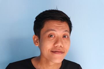 Funny tricky awkward smirk face of Asian young man in black t-shirt.