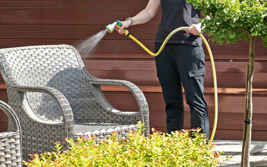 Anonymous cleaning, hose water washing wicker furniture from summer. Structures in backyard....