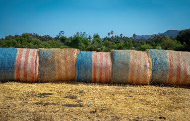 Bales of hay wrapped in American flags in a field against a blue sky