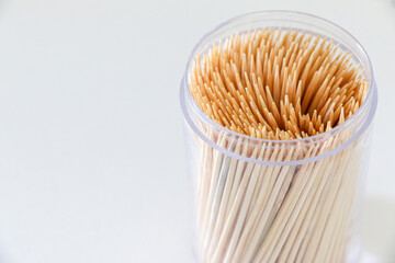 Close up of toothpicks in clear plastic container on right side of white table. Toothpicks are peaked small wooden sticks used to remove food and dirt from teeth. Dental hygiene. Copy space on left.