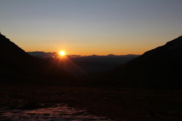 The golden sun rays extend above high mountain peaks casting a warm glow on the dark valley below....