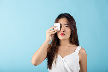 Fototapeta premium Facial Beauty Treatment Hygiene skin. Asian beautiful young woman removing cosmetic make up using pad cotton face cleaner disc, studio shot isolated on blue background, Happy female cleaning eyes