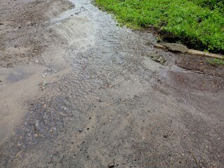 A small stream formed after heavy rain flows along the asphalt road and flows into a ditch. The...