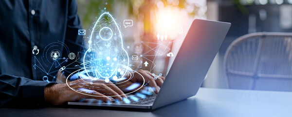 Man with laptop and blue hologram of rocket with business icons