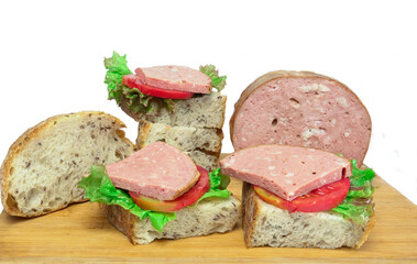On a wooden board sandwiches made of whole grain bread with tomato slices, pieces of sausage, lettuce leaves, close-up, on a white background.