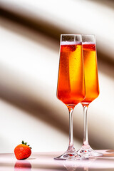 Strawberry festive cocktail drink with dry champagne, fruit puree and ice in glasses. Beige pink background, hard light