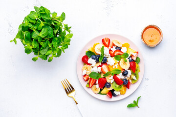 Fruity summer salad with fresh berries, ricotta cheese, banana, kiwi and mint, white background, top view