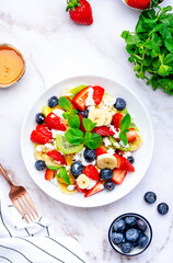 Fruit summer salad with berries, ricotta cheese, mint and honey, white marble background, top view