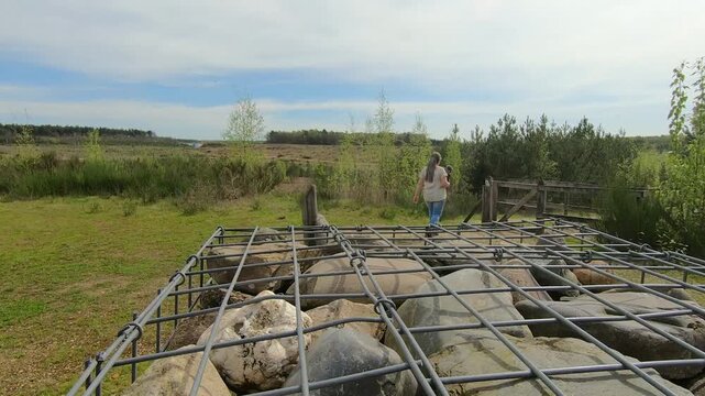 Tilt up shot of caged stone wall, hiker walking towards entrance to Mechelse Heide nature reserve, plain in background, Hoge Kempen National Park, sunny day in As, Limburg, Belgium