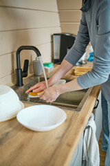 Unrecognizable man washing dishes in sink using sponge
