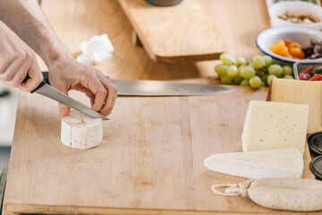 Close-up of hands slicing cheese on wooden board