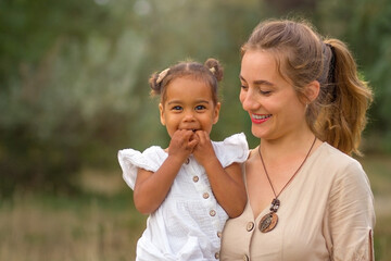 Mother and child. A happy African-American daughter in the arms of a white mother. Mothers Day.