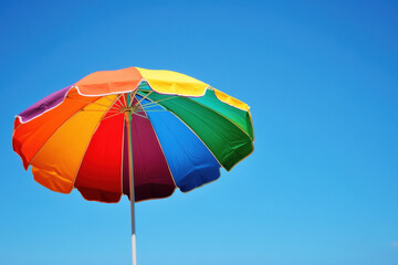 Obraz premium Bright and colorful rainbow beach umbrella against a clear blue sky. Perfect for summer, vacation, and outdoor activities.