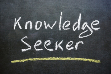 Close-up of the phrase Knowledge seeker written in chalk on a blackboard. Pursuit of learning concept.