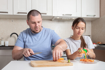 Teenage girl and father cooking at the kitchen, peeling and cutting ingredients, having fun together.