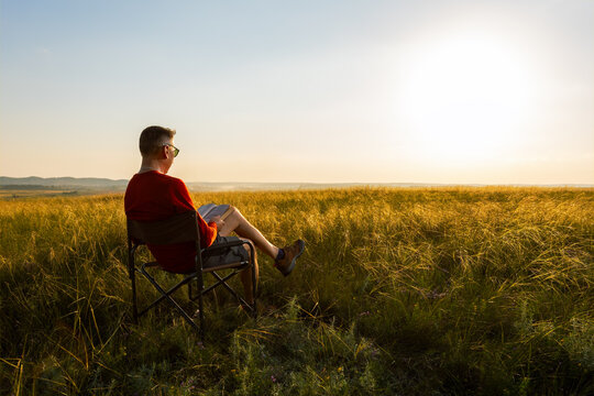 man sitting on an outdoor chair at nature and enjoying reading a book. - Powered by Adobe