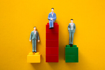 Three businessmen figurines are standing on different level block towers representing the concept...