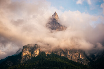 Clouds engulf a rugged mountain peak at sunset in a tranquil landscape