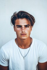Obraz premium Young man with stylish hair and necklace poses against a plain background