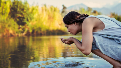 Fototapeta premium Young woman drinks water from the river