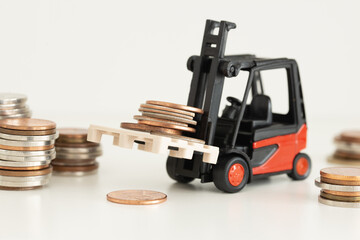 Miniature forklift truck carrying piles of coins, money and business financial concept