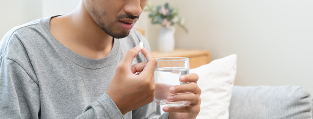 Young man taking painkiller and drink water to healing from cold flu.