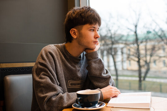 Young handsome man 20-22 year old reading book and drinking coffee in cafe. Generation Z.