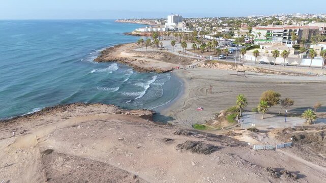 Drone captures a steady shot of the Cala Mosca area at Playa Flamenca, highlighting the beautiful contrast between the rugged landscape and the bustling urban backdrop along the Orihuela coast, Spain.