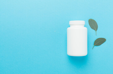 Bottle with pills and green leaves on color background, top view