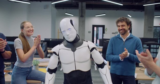 Camera moving closer while keeping focus on white modern bionic person. Creators surrounding robot and clapping with their hands. Automated gadget performing moves. Trying to look similar to person.