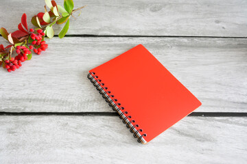 a red notebook with a red cover on a wooden table with a barberry branch 