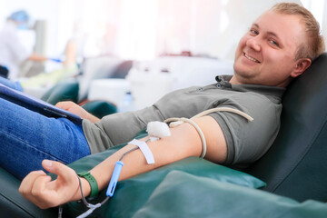 A young man sits comfortably in a medical facility and donates blood during a public event. He...