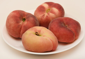 Flat peaches on a white plate. Delicious yellow peaches.
