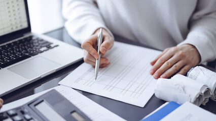 Woman accountant using a calculator and laptop computer while counting taxes for a client. Business...