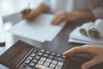 Woman accountant using a calculator and laptop computer while counting taxes for a client. Business...