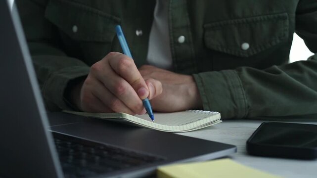 An office worker sits at a table with a laptop and takes notes in a notepad.
Business man, businessman at work