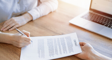 Business people signing contract papers while sitting at the wooden table in office, closeup. Partners or lawyers working together at meeting. Teamwork, partnership, success concept