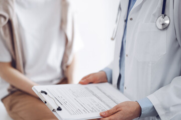 Doctor and patient discussing perfect health exam results. Friendly physician keeping with hands clipboard with medical papers near young woman. Medicine concept