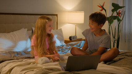 Happy Caucasian kids little siblings smiling family brother boy son daughter girl children watching online video enjoying cartoon movie using modern tech pc laptop computer bed indoors evening bedroom