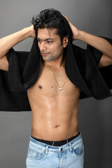 Fototapeta premium Cropped view of a young shirtless athlete with black towel after shower, bath or sauna. Indian bodybuilder with happy, mischievous facial expressions posing for camera