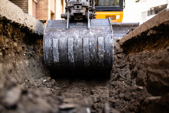 Close up view of excavator bucket digging ground on construction site.